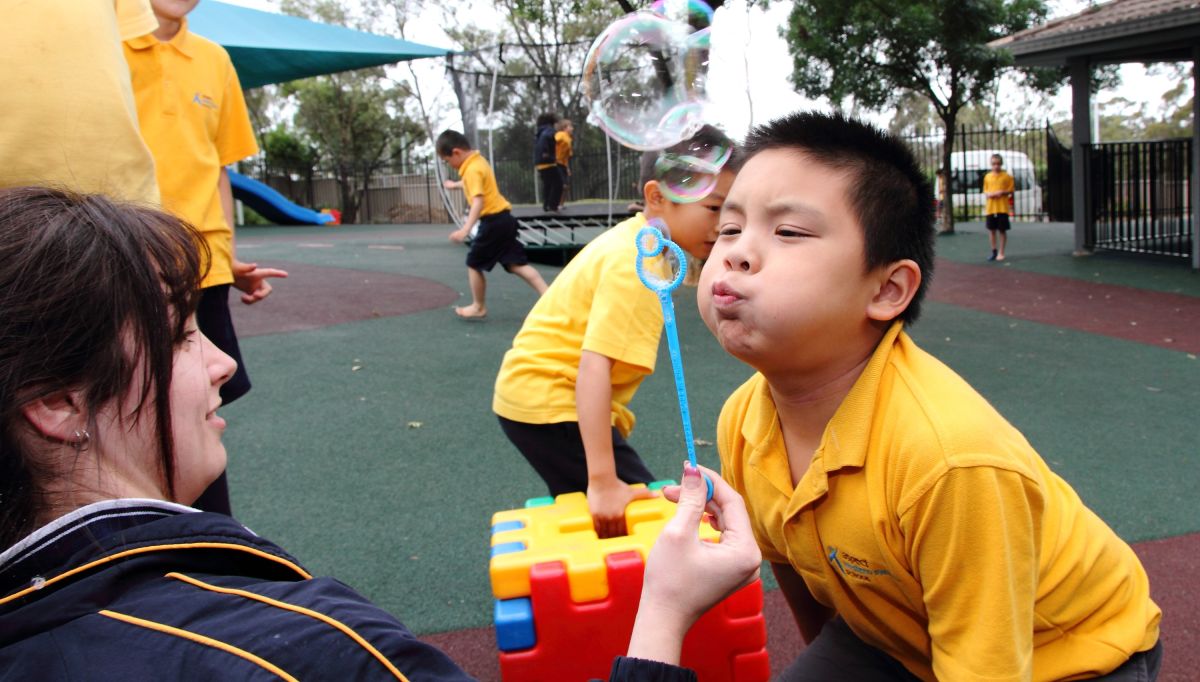 A student blows bubbles with a teacher within the playground at Western Sydney School
